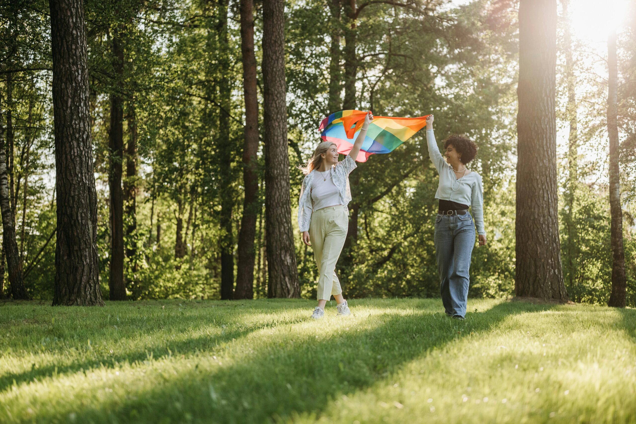 Två kvinnor som håller en prideflagga i skogen